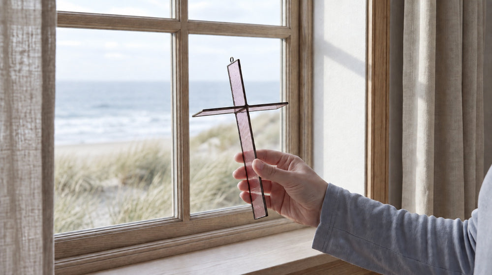 Rose Mist cross held in a hand by a coastal window